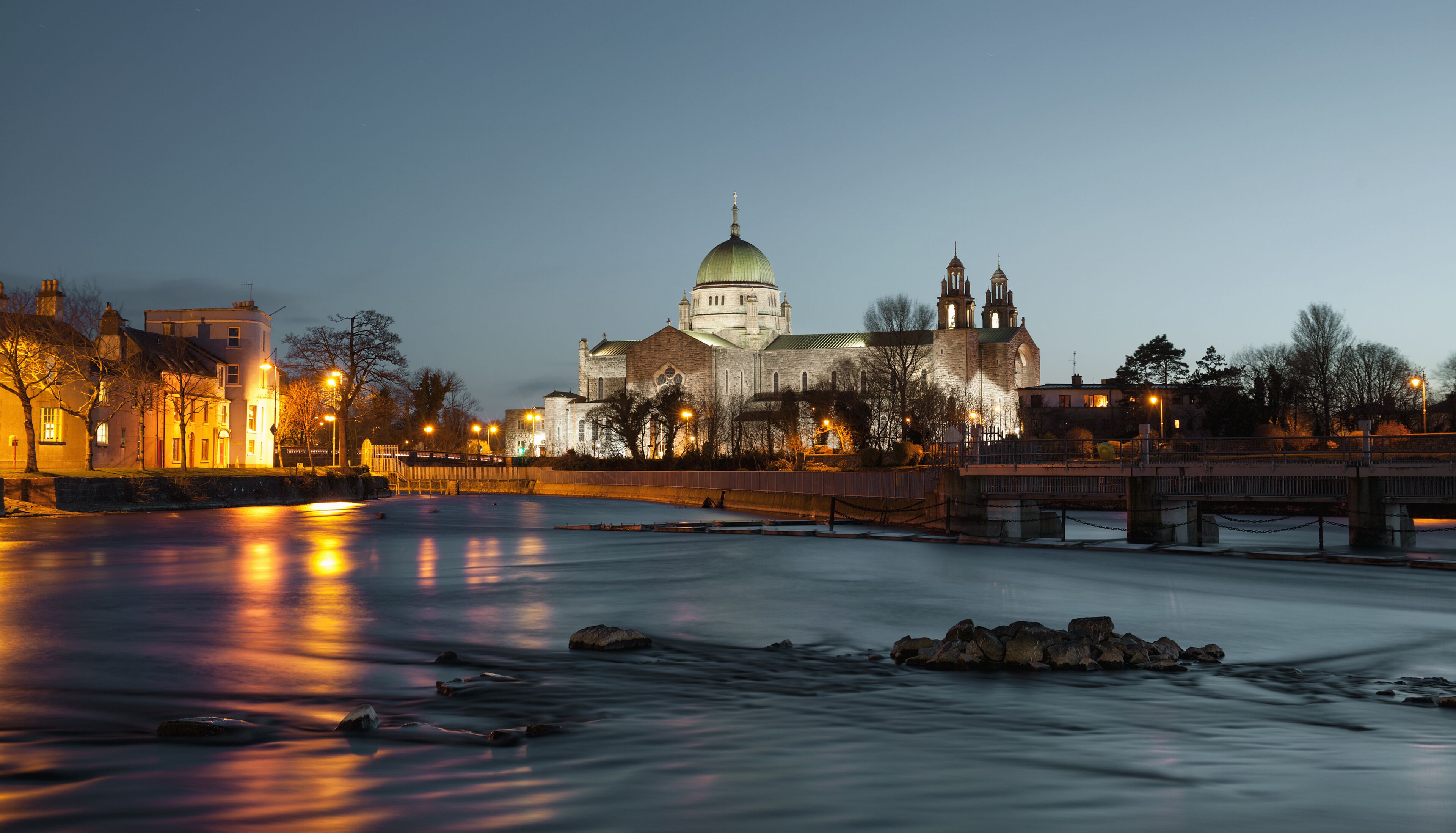 A river with a bridge, a stone building with a dome, and a church with towers.