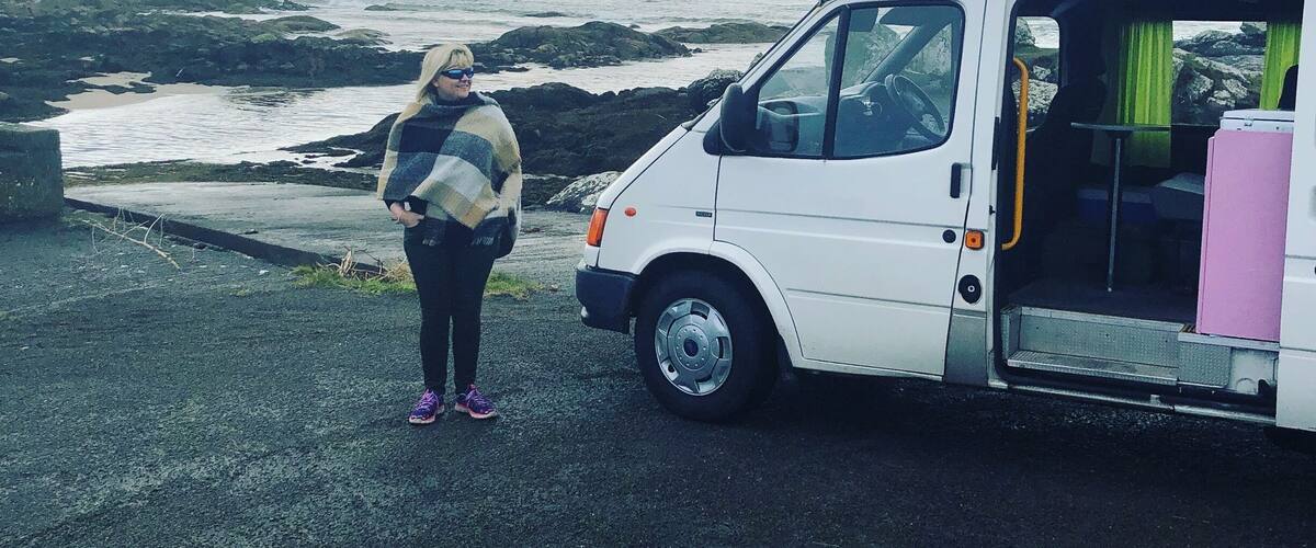 A person standing next to a white van with a pink cooler on the side.