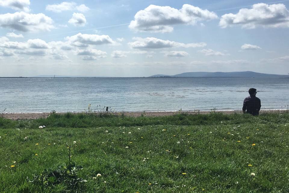 Een grasveld met iemand die op het gras zit, naar de zee gericht.