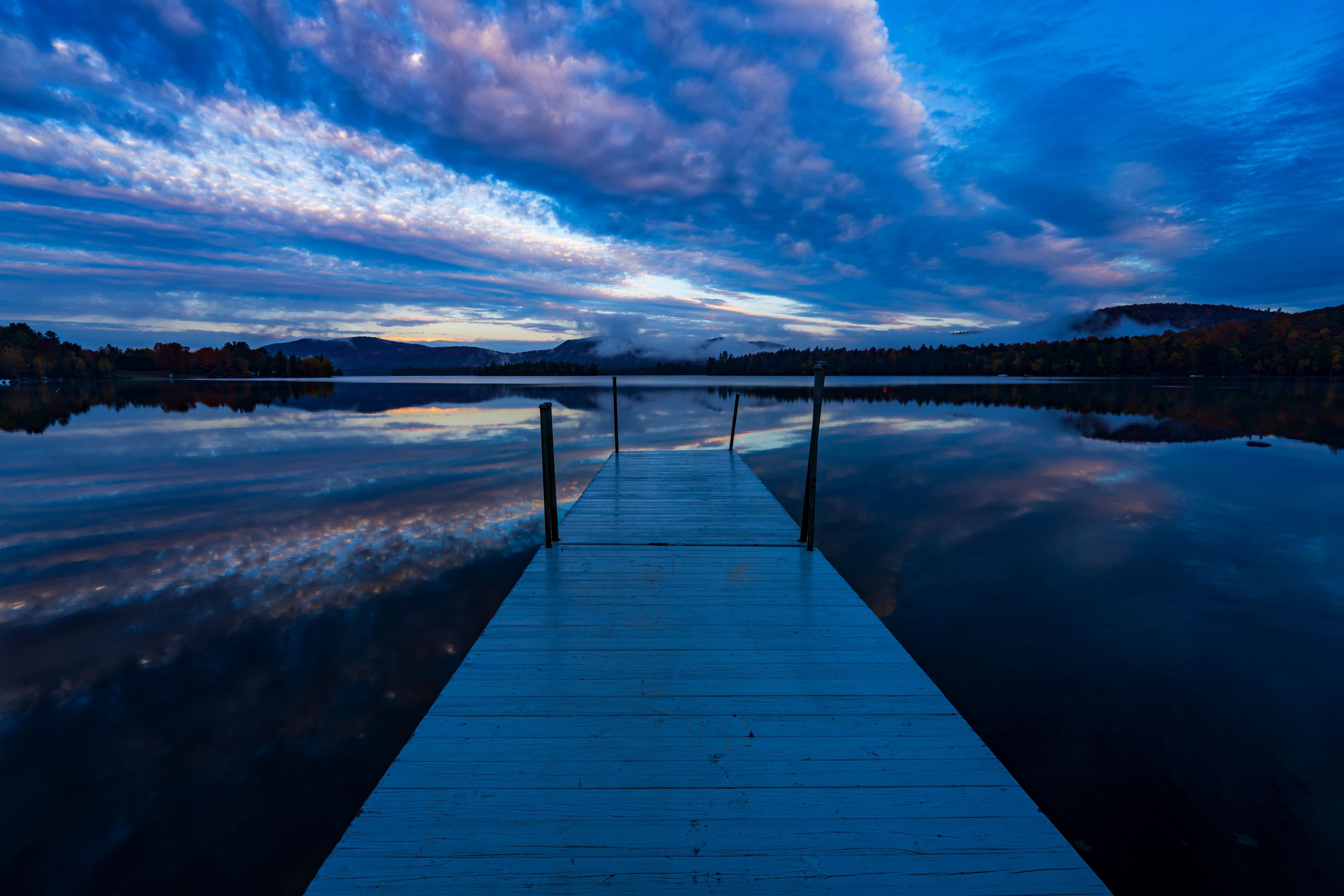 A wooden dock extending into a calm lake with a reflection of the sky and surrounding trees.