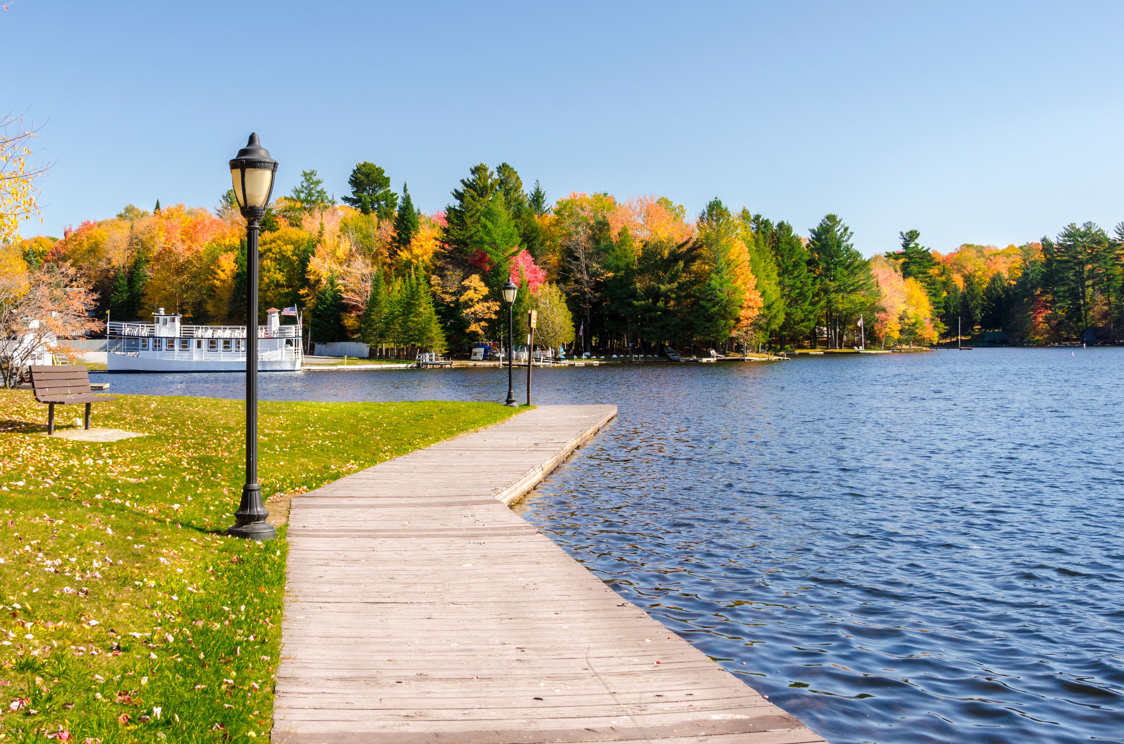 A wooden boardwalk leading to a lake with autumn-colored trees in the background.