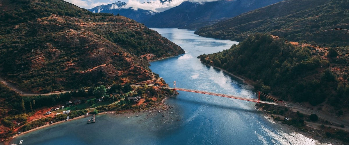 A river with a bridge, surrounded by mountains and greenery.