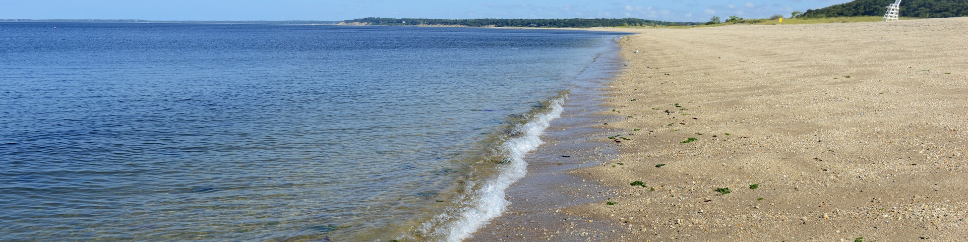 Una playa con agua cristalina, una orilla arenosa y una colina distante.