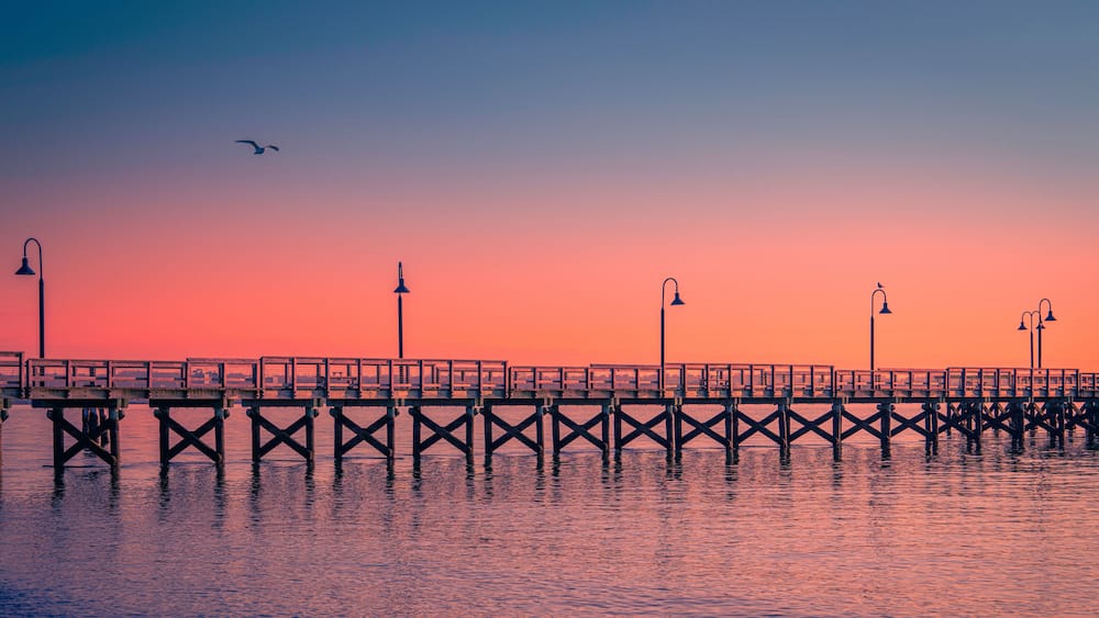 New England Seascape over Fishing Pier Boardwalk in New Haven Harbor in Connecticut at Sunrise: A tranquil beach walk spot with curving street light lamps and safety railing