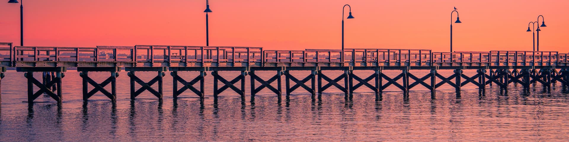 New England Seascape over Fishing Pier Boardwalk in New Haven Harbor in Connecticut at Sunrise: A tranquil beach walk spot with curving street light lamps and safety railing