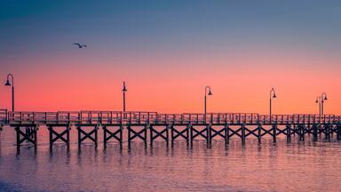 New England Seascape over Fishing Pier Boardwalk in New Haven Harbor in Connecticut at Sunrise: A tranquil beach walk spot with curving street light lamps and safety railing