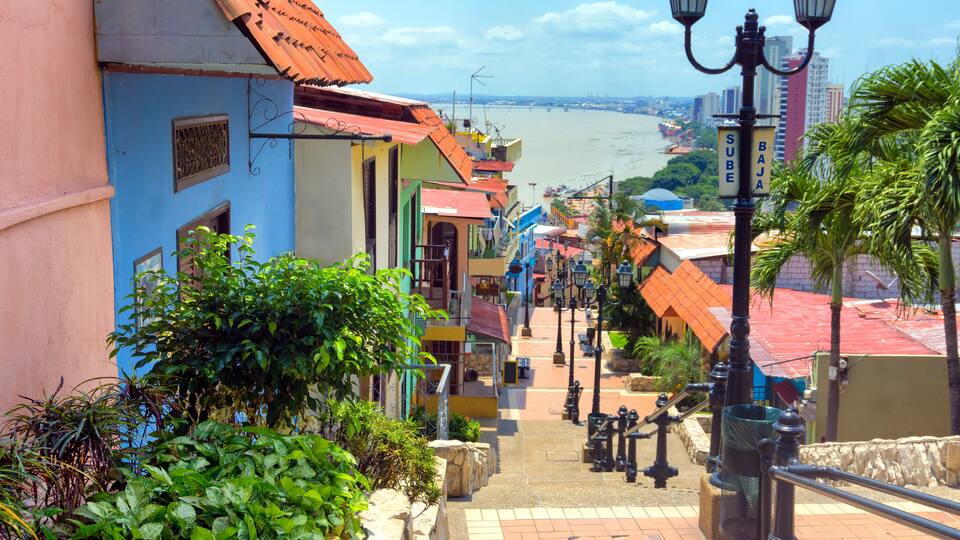 A colorful street with buildings, a river, and a bridge in the background.