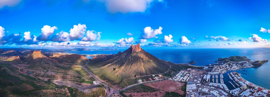Un pueblo costero con una montaña imponente, un puerto deportivo y una carretera sinuosa.