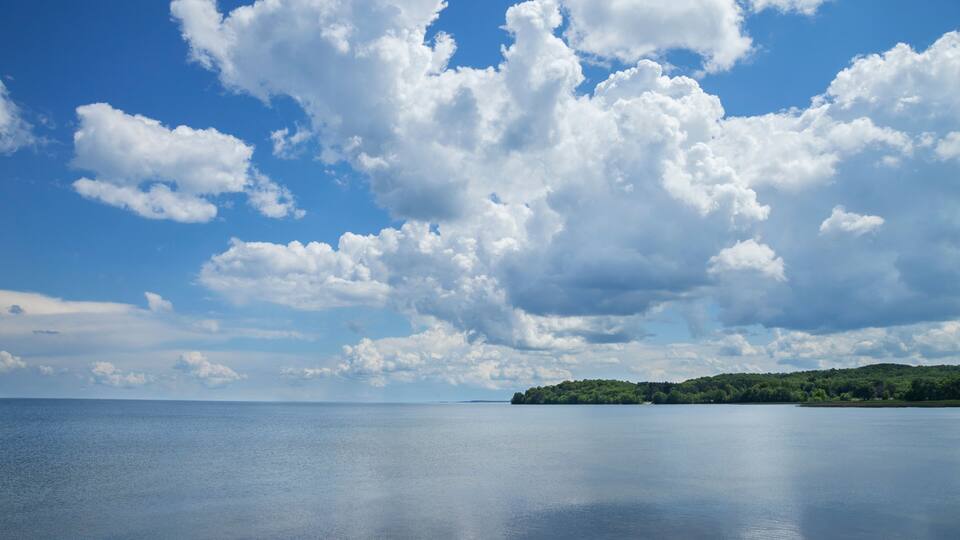 A calm sea with a clear sky and scattered clouds.