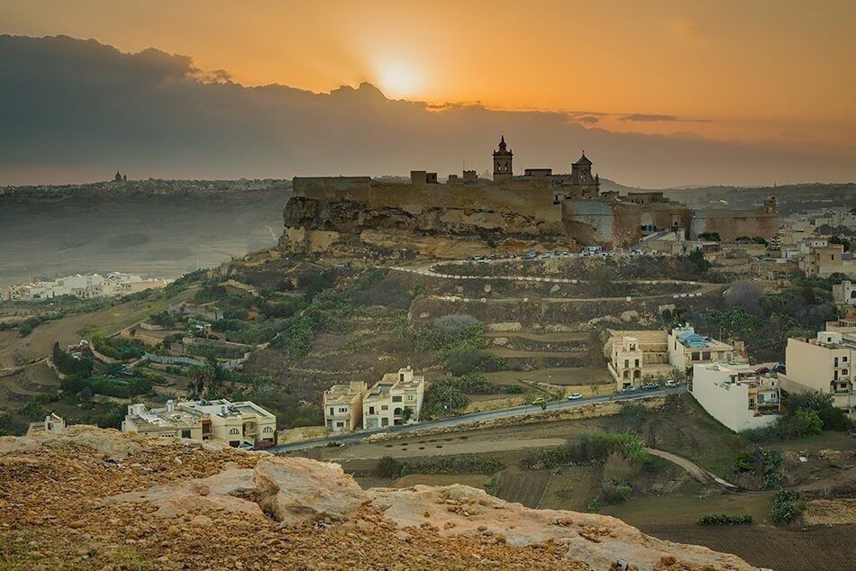 A coastal town with a prominent fortress-like structure, winding roads, and terraced fields.