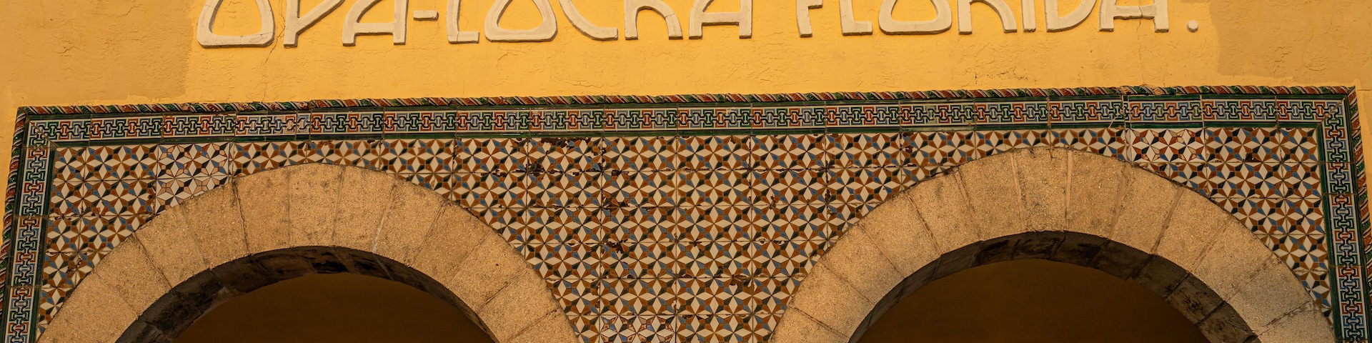 Fachada de um edifício com a inscrição "OPA-LOCKA FLORIDA" e duas grandes arcos com desenhos complexos em azulejos.