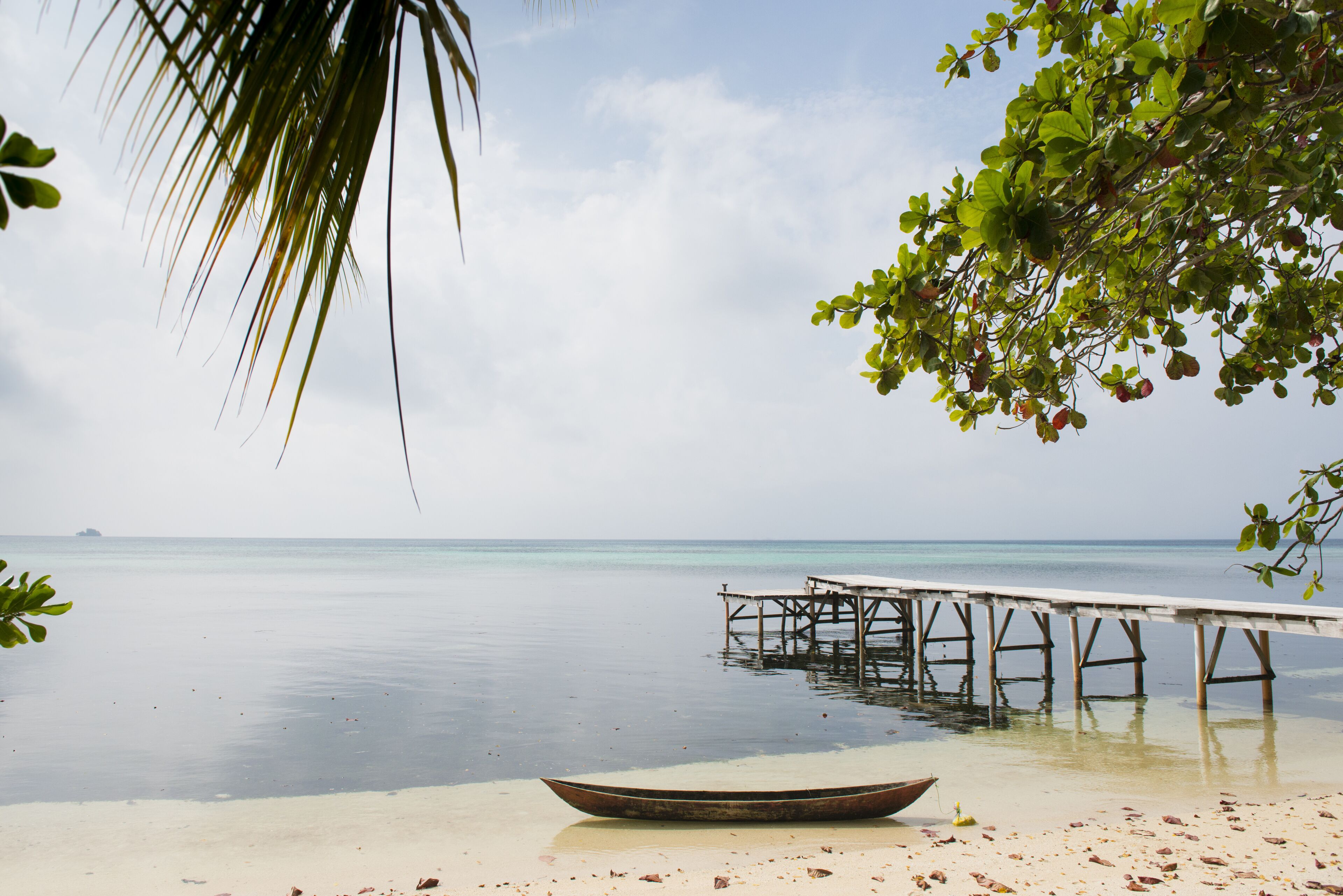 A boat on a sandy beach with a pier extending into calm turquoise waters.
