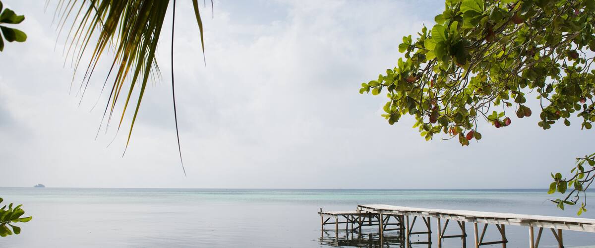 A boat on a sandy beach with a pier extending into calm turquoise waters.