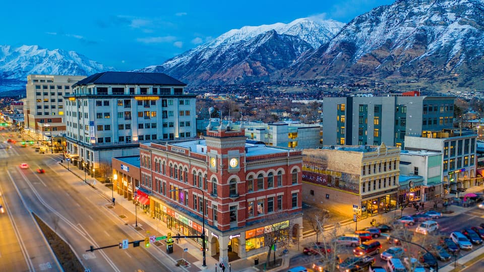 A cityscape with a prominent red building, a snow-covered mountain range, and a busy intersection.