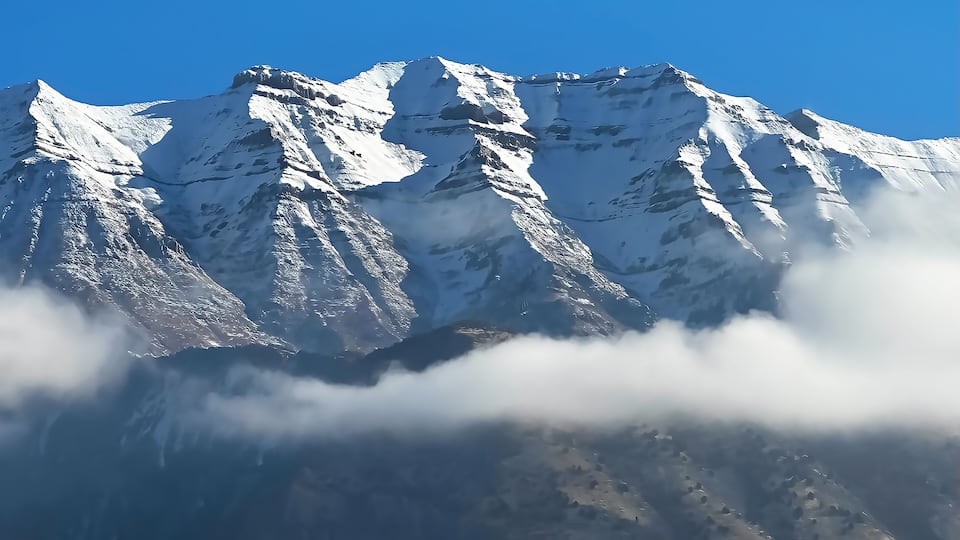 Snow-covered mountain peaks with a clear blue sky above and clouds at the base.