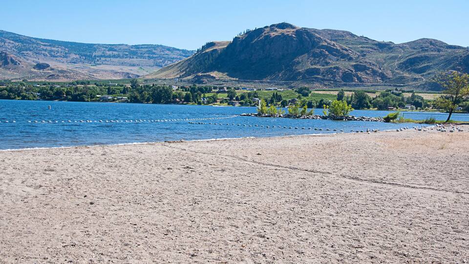 A sandy beach with a calm lake, a small island with rocks, and a mountain in the background.