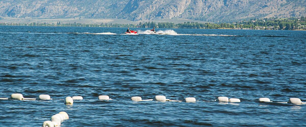 A lake with a red jet ski and buoys in the foreground, and mountains in the background.