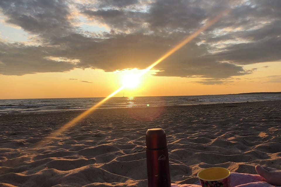 A beach with a sunset, sand, a thermos, and a cup.