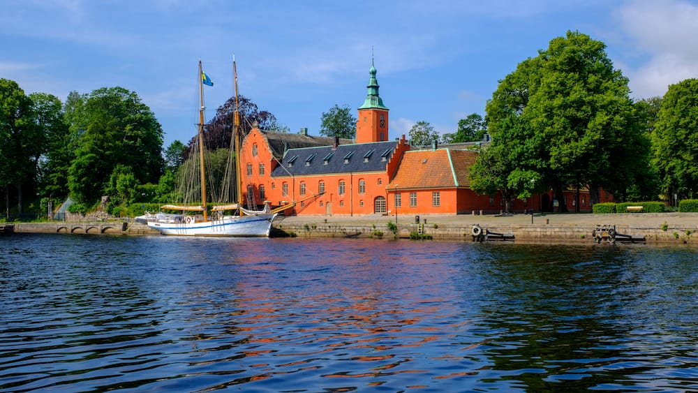 A historic building with a tower, a boat docked in front, and a calm river.