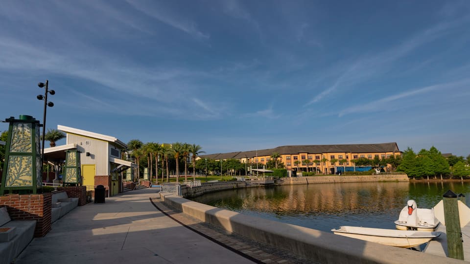 A waterfront promenade with a row of buildings, a swan on a dock, and a calm river.