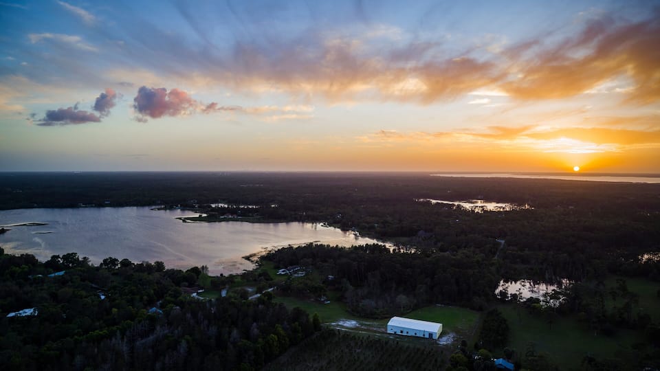 A sunset over a lake surrounded by forested hills and a small white building.