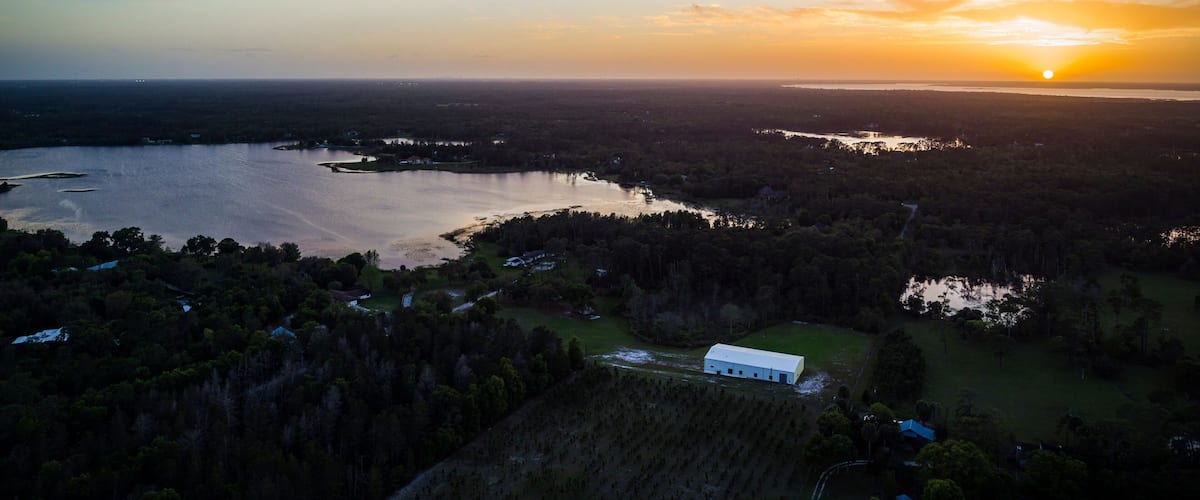 A sunset over a lake surrounded by forested hills and a small white building.