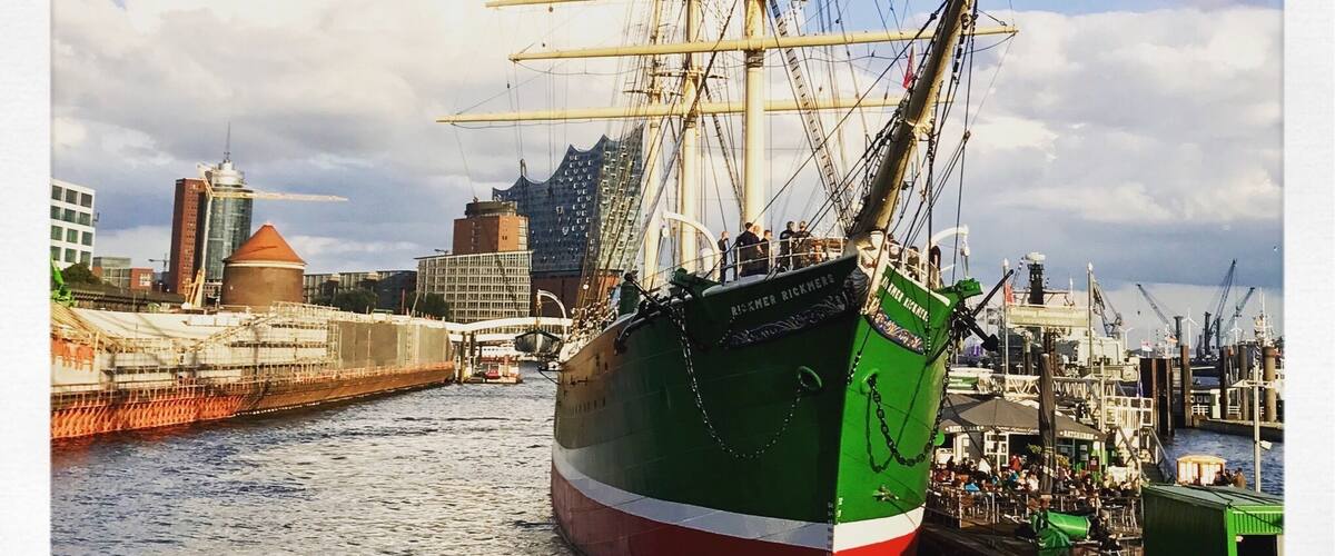 A tall ship docked at a harbor with a cityscape in the background.