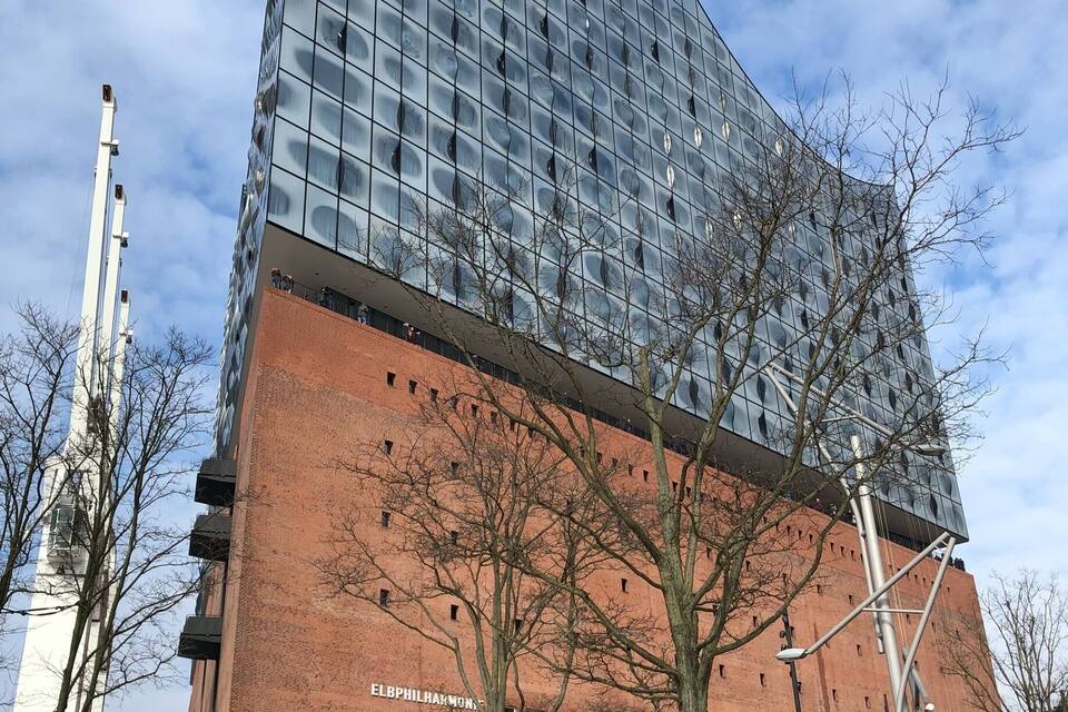 A modern glass building with a curved facade and a brick base labeled "ELBPHILAKMON."