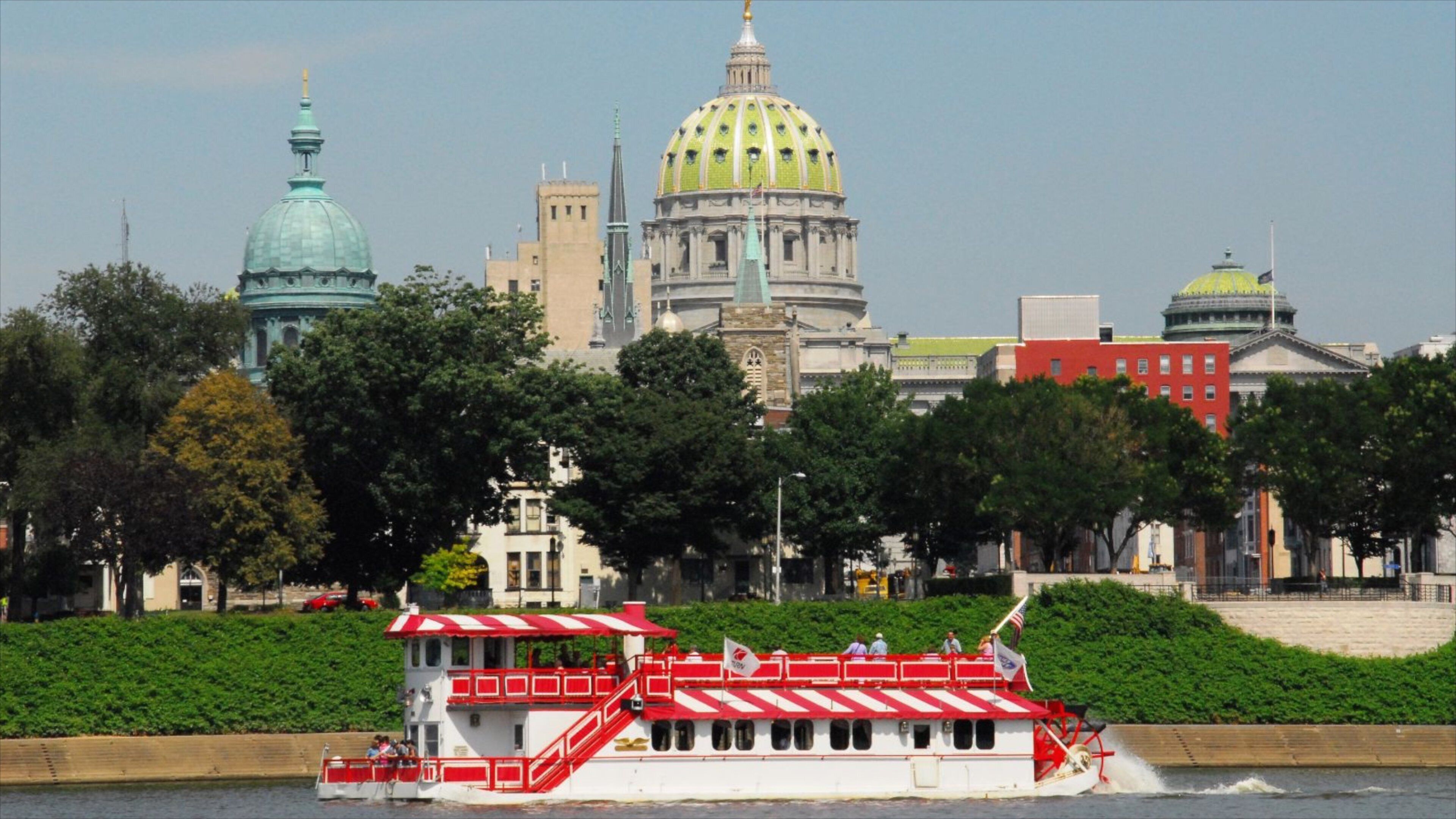 A riverboat with a red and white striped roof, a large green dome building, and a red building with a gold dome in the background.