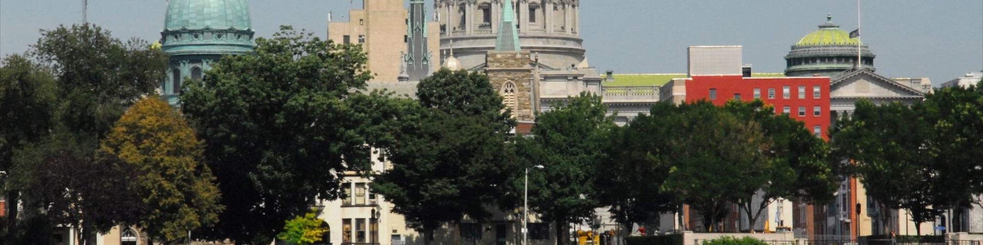 A riverboat with a red and white striped roof, a large green dome building, and a red building with a gold dome in the background.