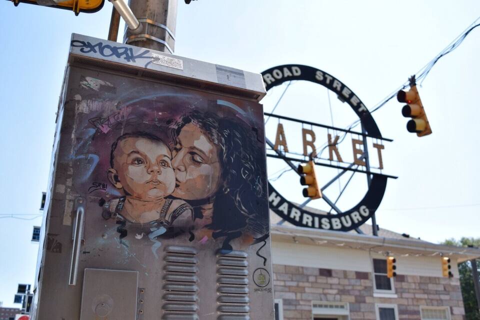 Un panneau de signalisation indiquant la direction de Harrisburg, avec une fresque représentant deux enfants peinte sur un coffret électrique.