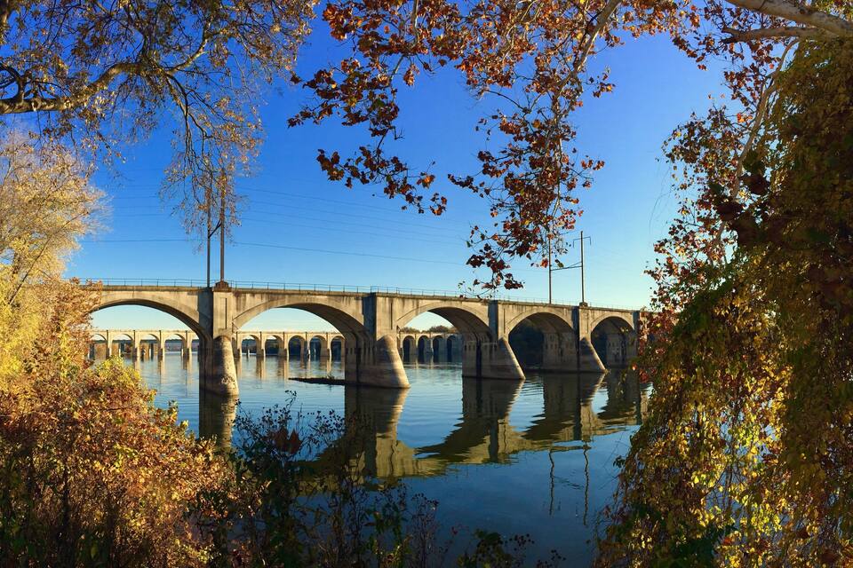 A stone bridge over a calm river, surrounded by autumn foliage.