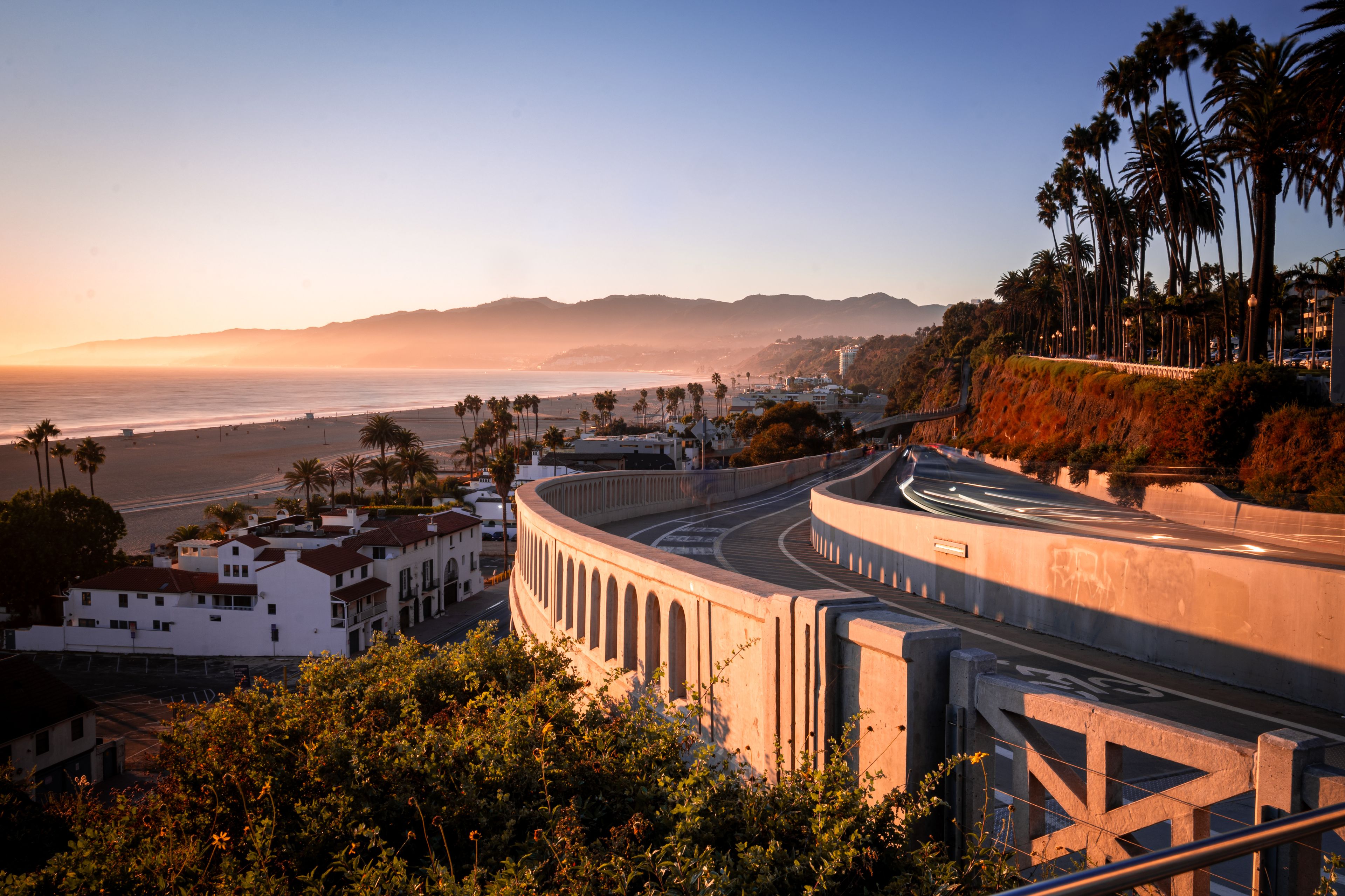 A coastal cityscape with a curved road, palm trees, and a beach in the background.