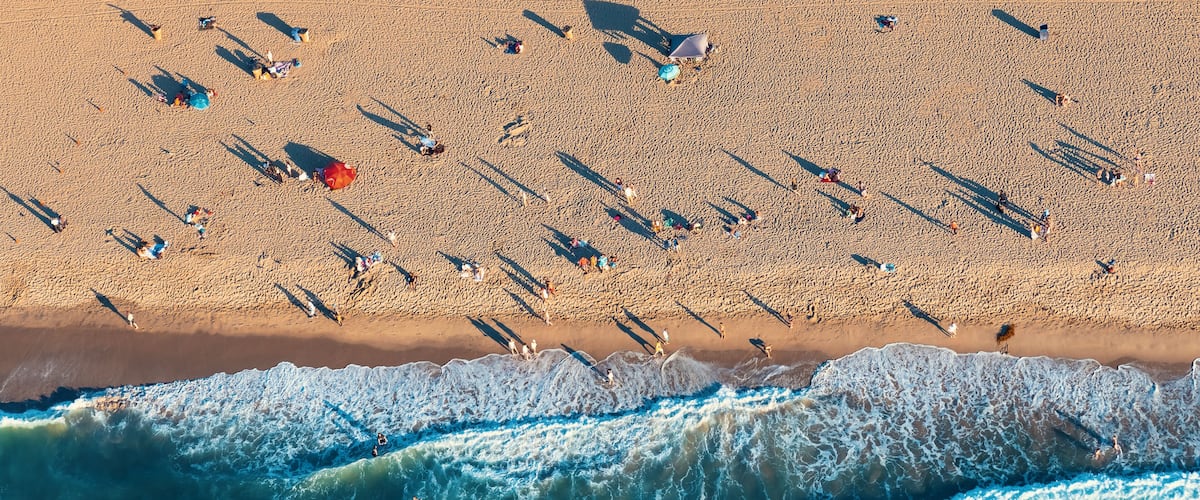 An aerial view of a beach with people, umbrellas, and waves.
