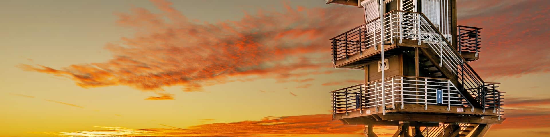 A lifeguard tower on a beach at sunset with people in the background.