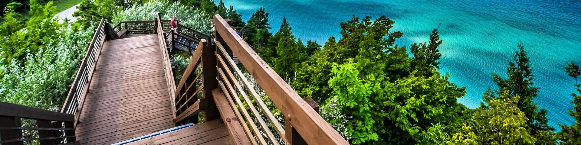 A wooden boardwalk leading to a coastal area with clear turquoise waters and a view of the horizon.