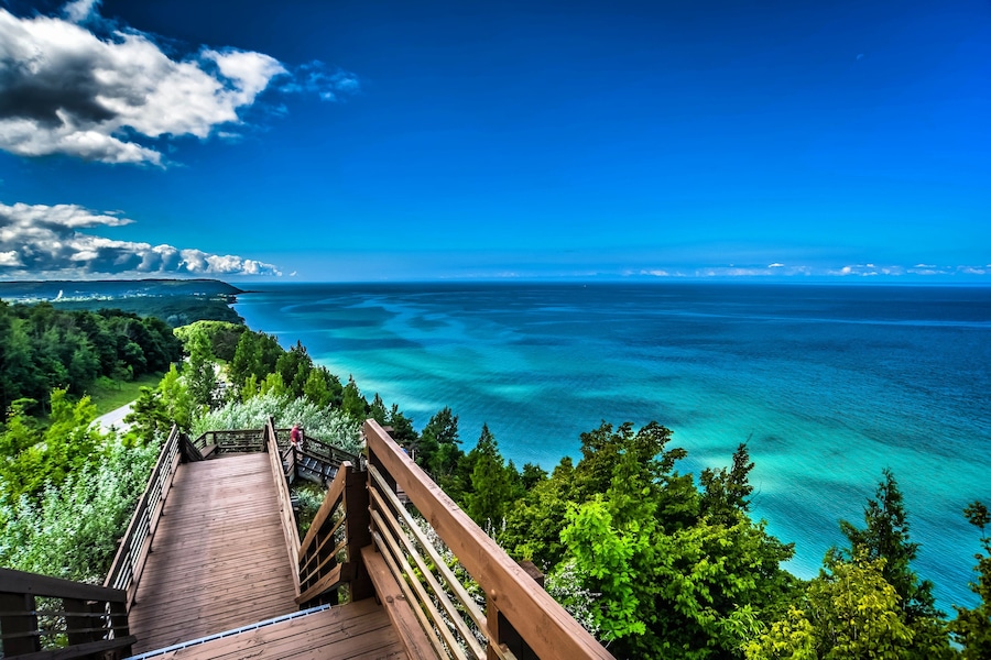 A wooden boardwalk leading to a coastal area with clear turquoise waters and a view of the horizon.