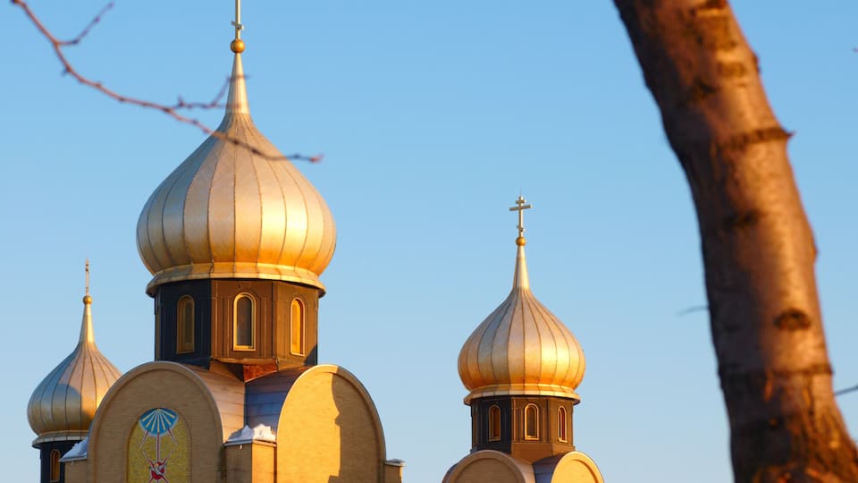 Golden domes of a church with a cross on top, set against a clear blue sky.