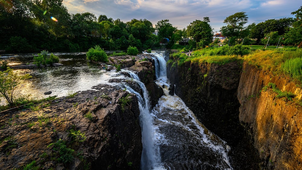 A waterfall cascading down a rocky gorge surrounded by lush greenery and trees.