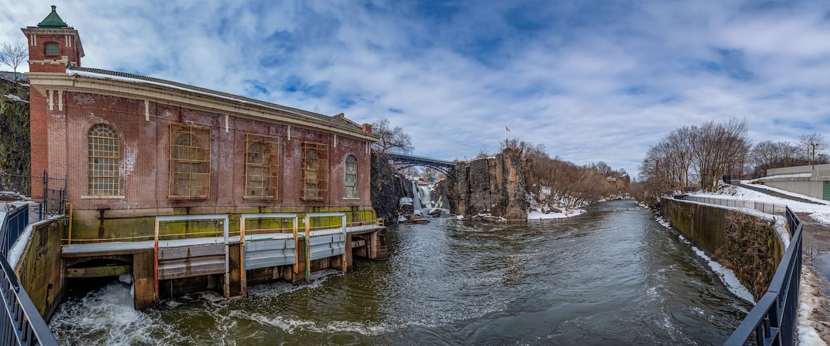 A river with a bridge, a brick building, and a waterfall.