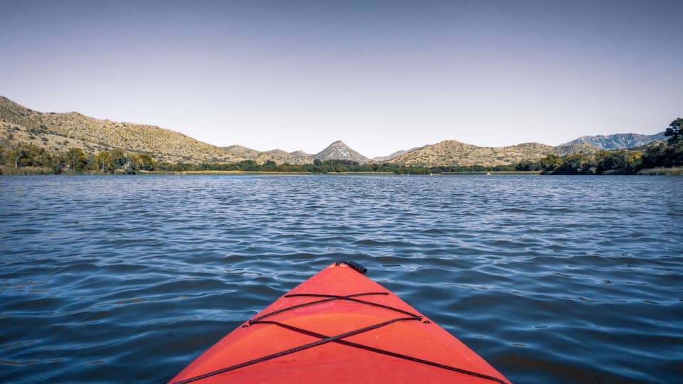 A red kayak on calm water with mountains in the background.
