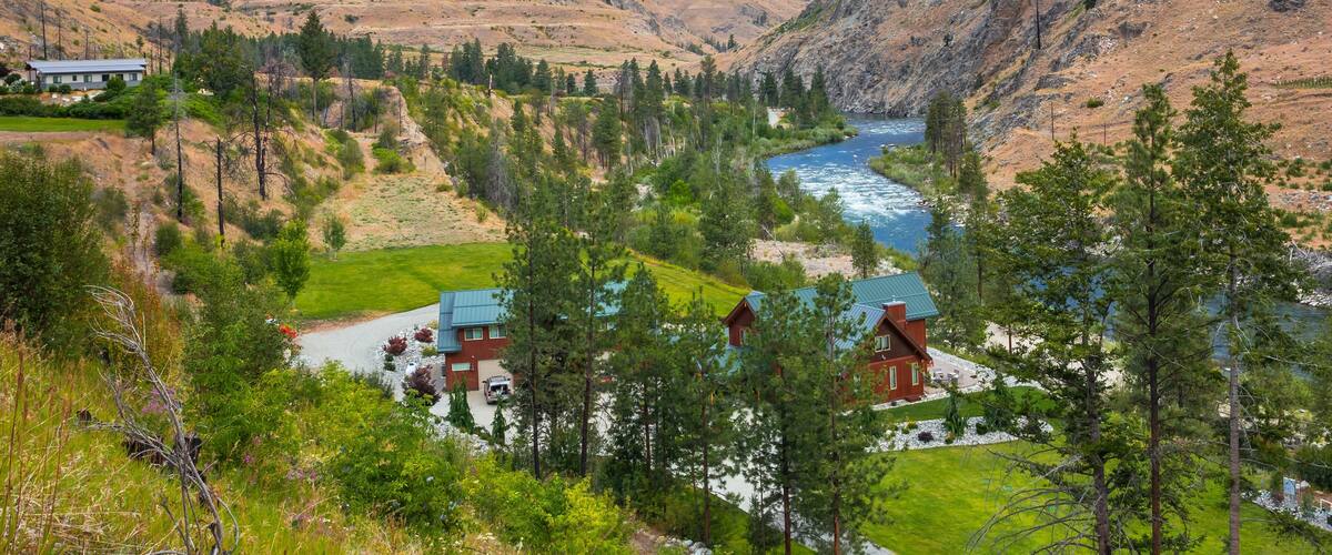 A river flowing through a valley with mountains in the background and houses with green roofs.