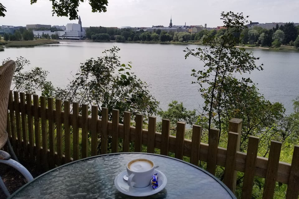 A table with a cup of coffee overlooking a lake with a cityscape in the background.