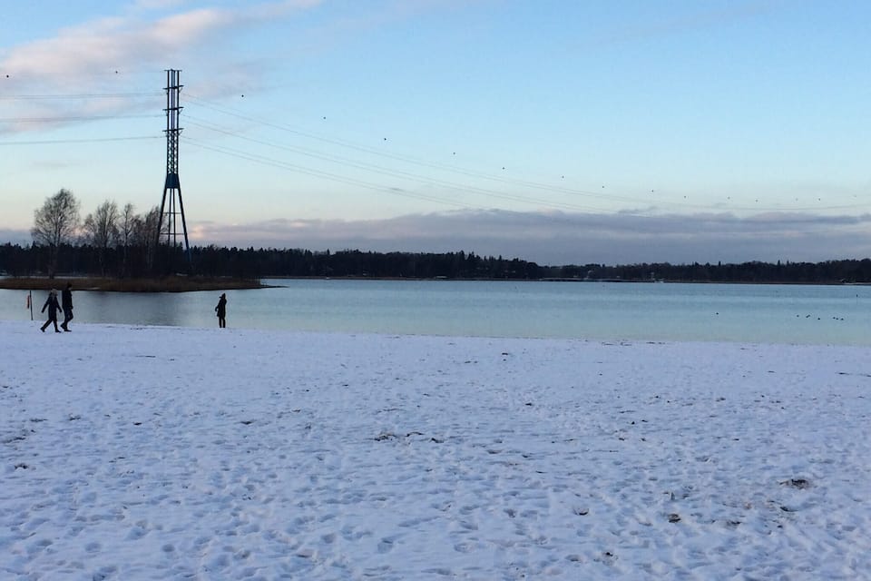 A snowy landscape with a calm lake, a tall metal structure, and a few people walking.