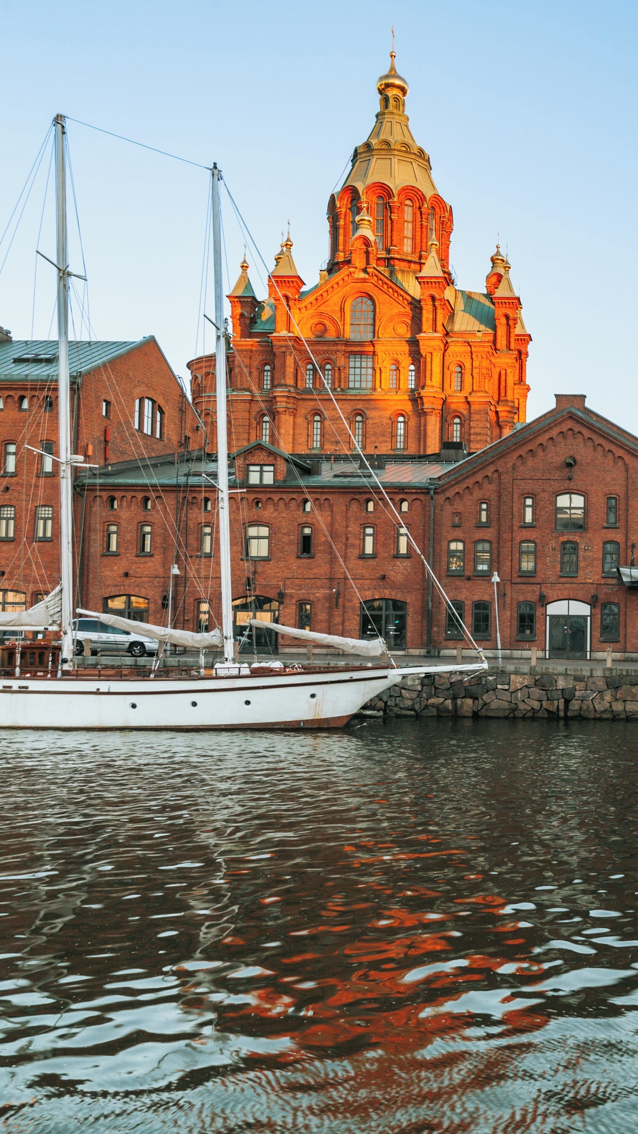 Uspenski Cathedral gleaming in the sunset light by the Katajanokka waterfront in Helsinki, Finland with historic architecture and serene waters