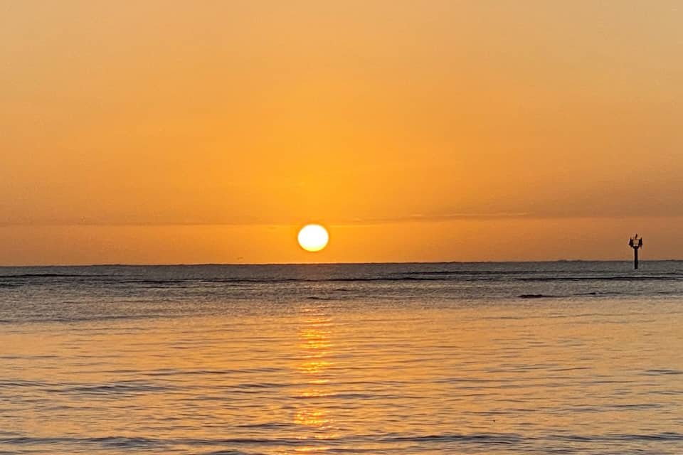 A sunset over the ocean with a lighthouse in the distance.