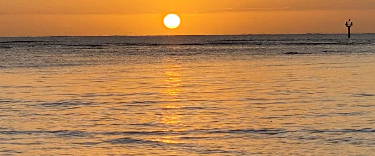 A sunset over the ocean with a lighthouse in the distance.