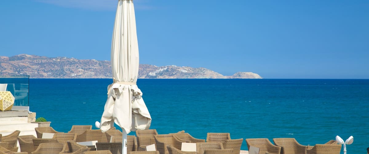 A seaside view with a white umbrella and wicker chairs.