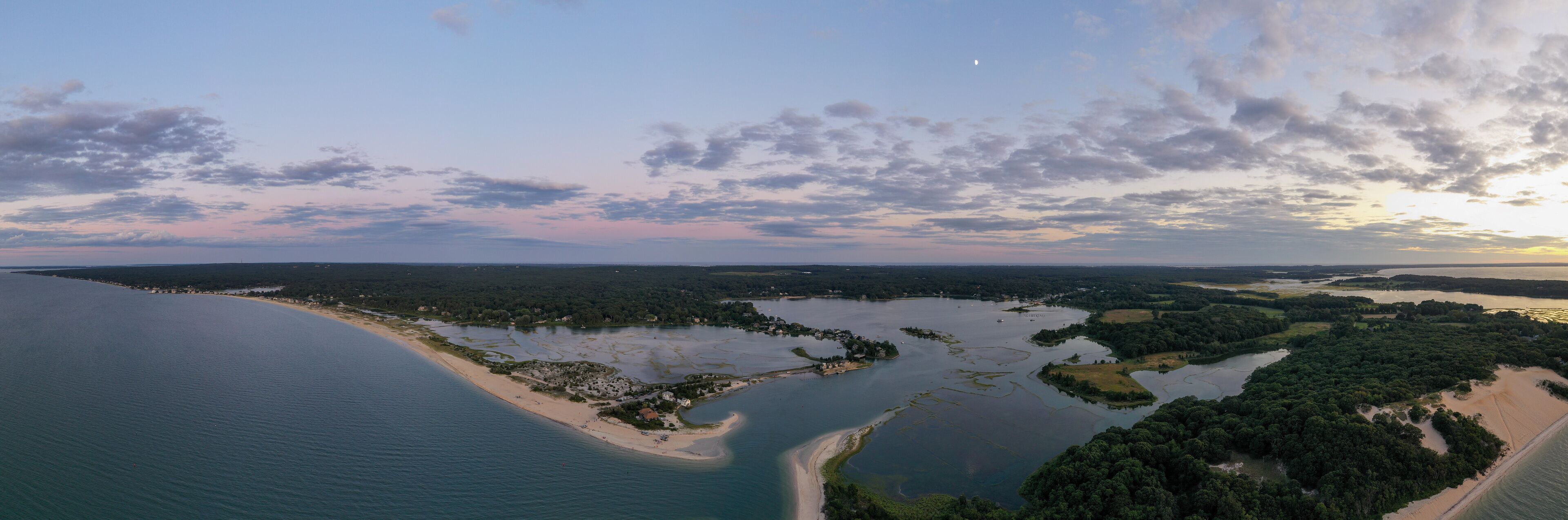 An aerial view of a coastal landscape with a sandy beach, a bay with small islands, and a dense forested area.