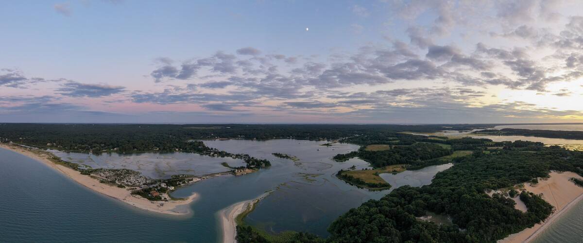 An aerial view of a coastal landscape with a sandy beach, a bay with small islands, and a dense forested area.